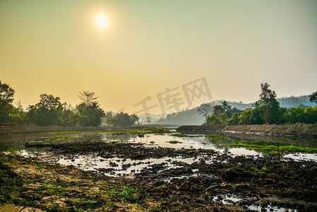 泥泞摄影照片_泥泞的沼泽，晨光中的日出，山的背景/亚洲乡村的湖