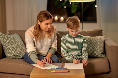 家庭、休闲和人的概念-母亲和小儿子在家里用彩色铅笔和纸画。家里拿着铅笔画的母子俩