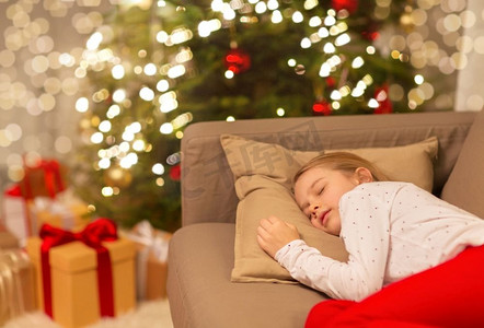 矢量树下的女孩摄影照片_圣诞节、假日和童年概念—女孩睡在家里的沙发上。女孩睡在沙发上在圣诞节