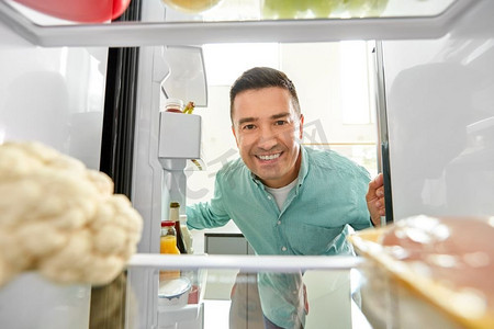 冰箱里的食物摄影照片_饮食与饮食理念--微笑的中年男子在厨房的冰箱里寻找食物。一名男子在厨房的冰箱里寻找食物