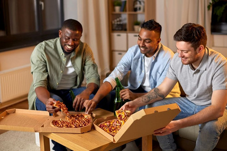 啤酒精美矢量摄影照片_友谊，食物和人的概念—快乐的男性朋友在家里喝啤酒和吃披萨。快乐的男性朋友与啤酒吃披萨在家里
