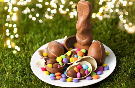 复活节，糖果和糖果的概念盘，上面有巧克力兔，鸡蛋和草地上的糖果。巧克力兔，鸡蛋和糖果放在盘子里