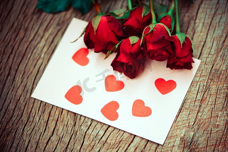 红玫瑰花束浪漫的爱情人节卡片信封信件邮件与红心/邀请卡婚礼在木背景 