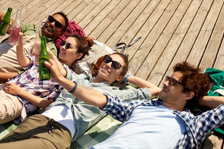 休闲，野餐和人的概念—朋友喝啤酒和苹果酒在木露台在夏天。朋友喝啤酒和苹果酒在木露台
