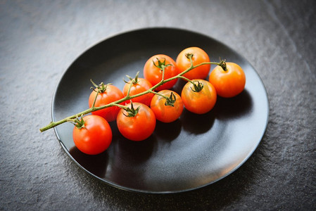 成熟的红色番茄藤在桌子上的熟食/新鲜番茄的分支在黑色盘子有黑暗背景