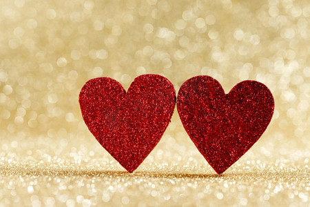 两个小手工制作的红色闪光心脏在明亮的金光bokeh背景情人节卡。两颗心在散景背景