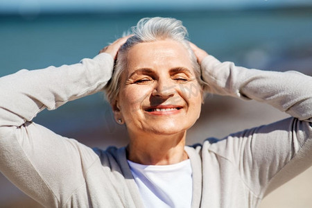 人与休闲理念--幸福老太太沙滩晒太阳写真。老年妇女在海滩上晒太阳的肖像