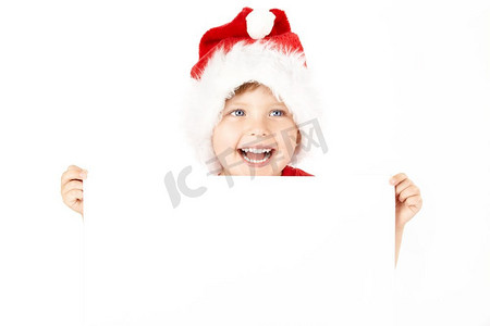 戴圣诞帽的男孩摄影照片_戴圣诞老人帽的男孩拿着白纸