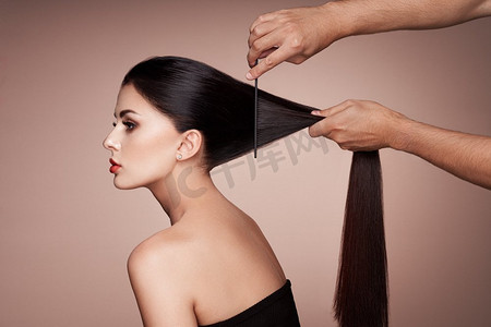 睫毛摄影照片_理发师给女人梳头。美丽的年轻女子剪发的肖像。护理长而光滑的头发