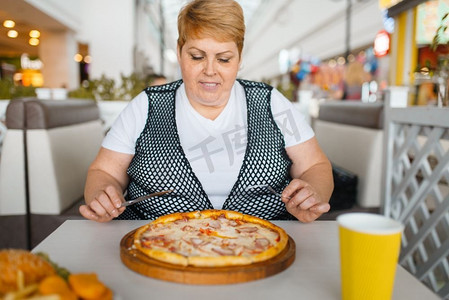 在快餐店吃披萨的胖女人。超重的女性人在桌子上与垃圾晚餐，肥胖问题