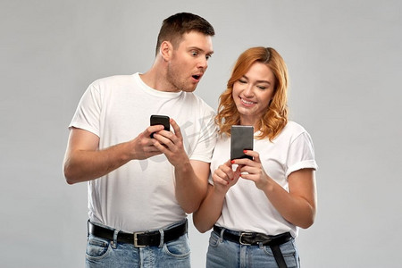 技术和人的概念—愉快的夫妇在白色t恤与智能手机在灰色背景。快乐的夫妇在白色T恤与智能手机