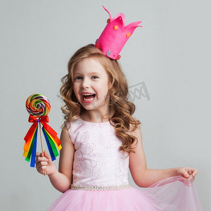 美丽的小糖果公主，戴着皇冠，手里拿着大棒棒糖，微笑着。戴皇冠的女孩拿着棒棒糖