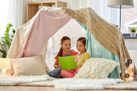 童年，hygge和友谊概念—快乐的女孩读书在孩子帐篷或帐篷在家里。快乐的女孩读书在孩子们帐篷在家里