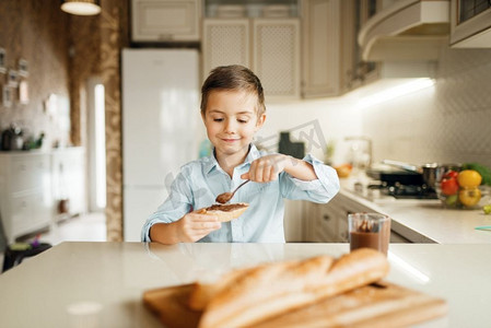 小男孩把融化的巧克力涂在面包上。可爱的男孩在厨房做饭。快乐的孩子准备和品尝甜甜点在柜台