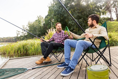 休闲与人的概念—快乐的朋友在码头钓鱼和喝啤酒。快乐的朋友钓鱼和喝啤酒在码头