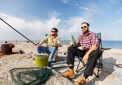 休闲与人的概念-快乐的男性朋友在海边钓鱼，喝啤酒。男性朋友在海边钓鱼和喝啤酒