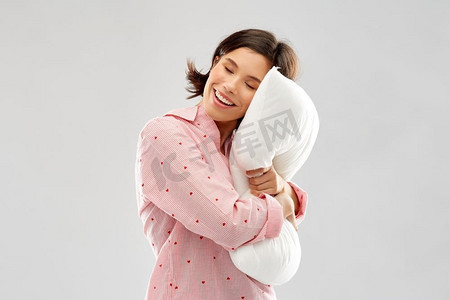 人和就寝时间概念—睡衣拥抱枕头愉快的年轻妇女在灰色背景快乐的年轻女人在睡衣拥抱枕头