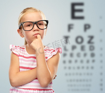 视力和视觉概念—可爱的小女孩在黑眼镜在眼睛测试图表背景。小女孩在眼镜超过视力测试表