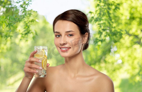 美容排毒概念-在绿色自然背景下饮用加柠檬和冰块的淡水。喝加柠檬和冰的水的女人