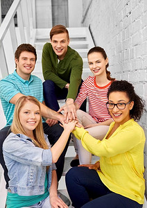 友谊和人的概念-微笑的青少年朋友或学生在楼梯上伸出手。十几岁的朋友或学生握手