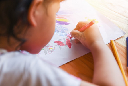 彩色铅笔摄影照片_女孩在家里的木桌上用彩色铅笔在纸上作画/孩子在画素描和彩色蜡笔