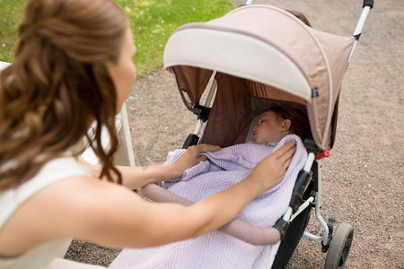 家庭、母亲和人的概念-在夏季公园，母亲用毯子盖着婴儿车里的孩子。在夏令营推着婴儿车的母亲