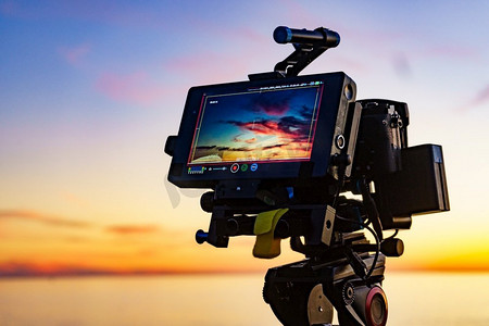 相机旅行摄影照片_专业摄像机在三脚架拍摄照片电影视频日落在海上。相机拍摄的日落在海上的照片