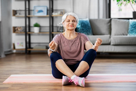 运动、健身和健康的生活方式理念--快乐的老年女性在家中的运动垫上冥想。快乐的老年妇女在家中的垫子上冥想