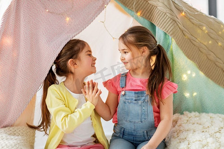 童年，hygge和友谊概念—快乐的女孩躺在孩子的帐篷和在家里谈话。快乐的女孩躺在孩子帐篷和谈话在家里