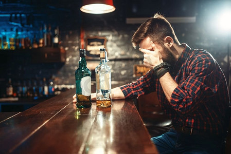 酗酒者坐在吧台边喝烈性饮料。酒吧中的男性，酗酒，醉酒