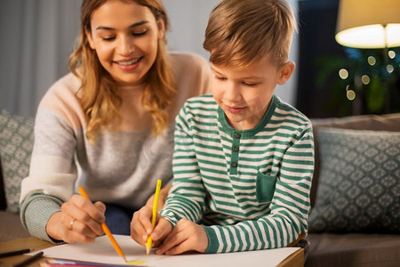 家庭，休闲和人的概念—母亲和小儿子与彩色铅笔和纸提请在家里。母亲和儿子与铅笔绘画在家里