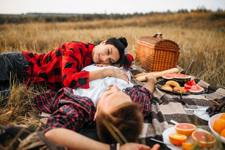 情侣躺在格子布上，夏日田野野餐。男人和女人的浪漫旅行。情侣躺在格子花呢上，夏日田野野餐