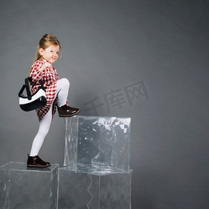 透明灰色背景摄影照片_一个戴着虚拟现实眼镜的小女孩在灰色背景下爬上透明的积木