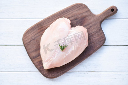 生鸡肉与迷迭香在木砧板/新鲜生鸡胸心形鱼片在木健康食品概念，顶视图 