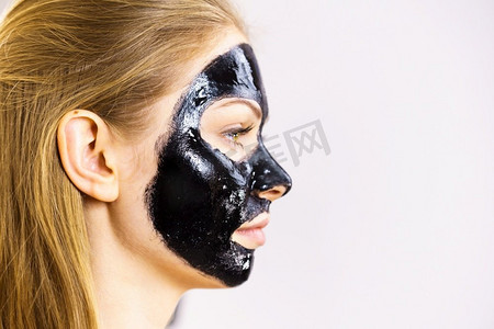 对面膜摄影照片_年轻女子与化妆品在脸上，碳水化合物排毒黑色剥离面膜。水疗护理。护肤侧视图。妇女与黑色剥离关闭面具在脸上
