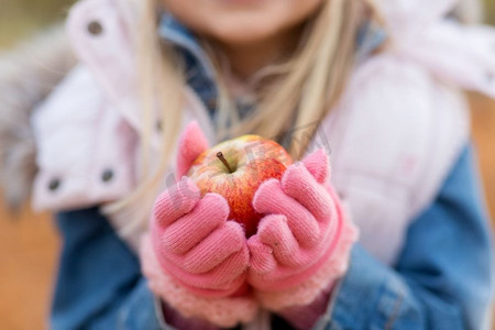拿着苹果摄影照片_童年、季节和自然的概念--小女孩在秋天拿着苹果的特写。小女孩在秋天拿着苹果的特写
