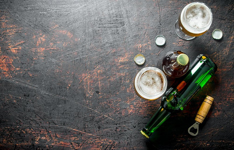 金色瓶子摄影照片_有开瓶器和盖的玻璃杯和瓶子里的啤酒。在乡村背景下。有开瓶器和盖的玻璃杯和瓶子里的啤酒。