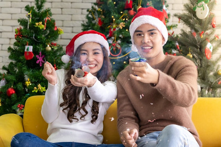 一对年轻的亚洲成年少年夫妇在装饰着圣诞树的客厅里一起放鞭炮庆祝圣诞节。
