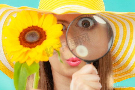植物学家妇女滑稽的脸表情在黄色帽子检查通过放大镜看花在蓝色背景