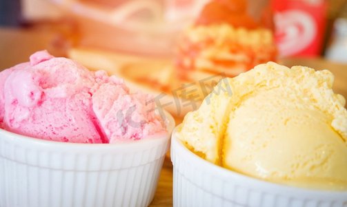 木质托盘上的冰激凌杯/桌子背景上的黄色香草和草莓冰淇淋勺