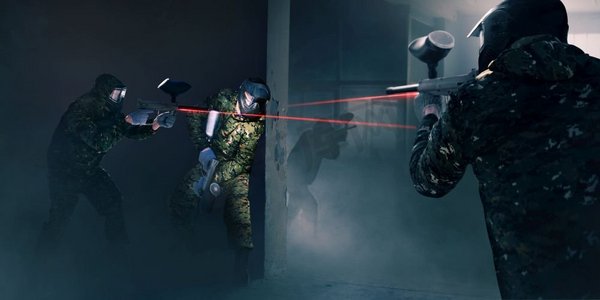 彩弹小组在战斗中，枪与激光瞄准器。极限运动游戏，戴着防护面具和迷彩服的选手手持武器