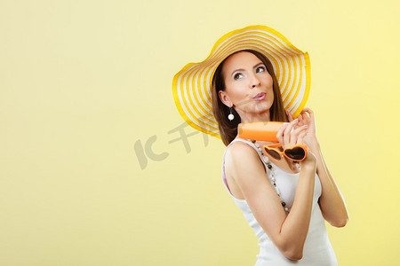 夏日文案摄影照片_假日夏日时尚。和护肤理念。戴着黄色帽子的女子手持心形太阳镜防晒霜，背景明亮的文案空间