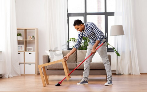 清洁、家务和家政概念—印度男子用扫帚扫地在家里。男人用扫帚打扫地板