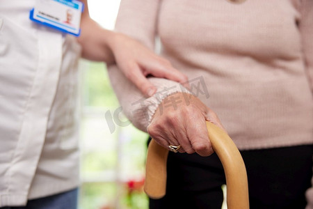 扶着拐杖的老年妇女在护理员的帮助下特写