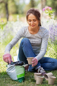 园艺和人的概念—快乐的年轻妇女填充罐与土壤在夏季花园。妇女在夏季花园用土填充花盆