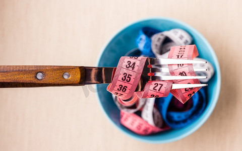 减肥食品健康生活方式和苗条身材概念。许多五颜六色的卷尺在蓝色碗在桌子上有叉子，顶视图