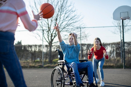 少年男孩在轮椅上打篮球与朋友