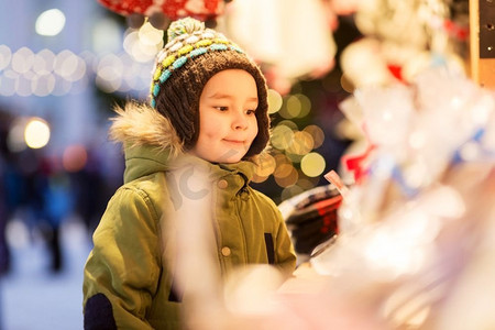 摊位摄影照片_假日，童年和人的概念—快乐的小男孩在圣诞市场摊位在冬天的晚上。快乐的小男孩在圣诞市场在冬天