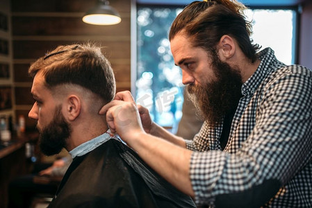 理发店理发摄影照片_理发师削减发型的客户人在黑色沙龙斗篷，理发店在背景