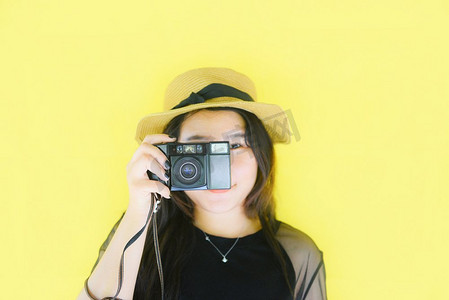 令人愉快的年轻亚洲妇女肖像时尚微笑和拍照有老式胶片照相机的摄影师在黄色背景/时髦酷女孩 